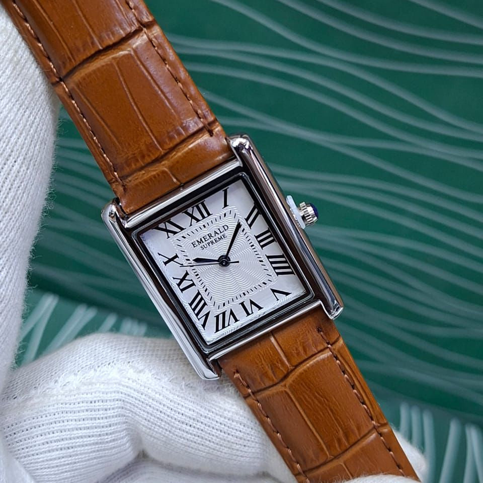 Watch with brown leather strap and white face held by a white glove against a green textured background