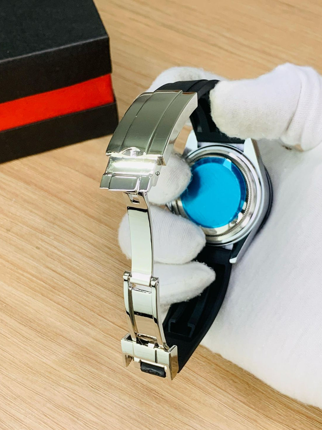 Watch with a blue face and silver band held by white gloves on a wooden surface.