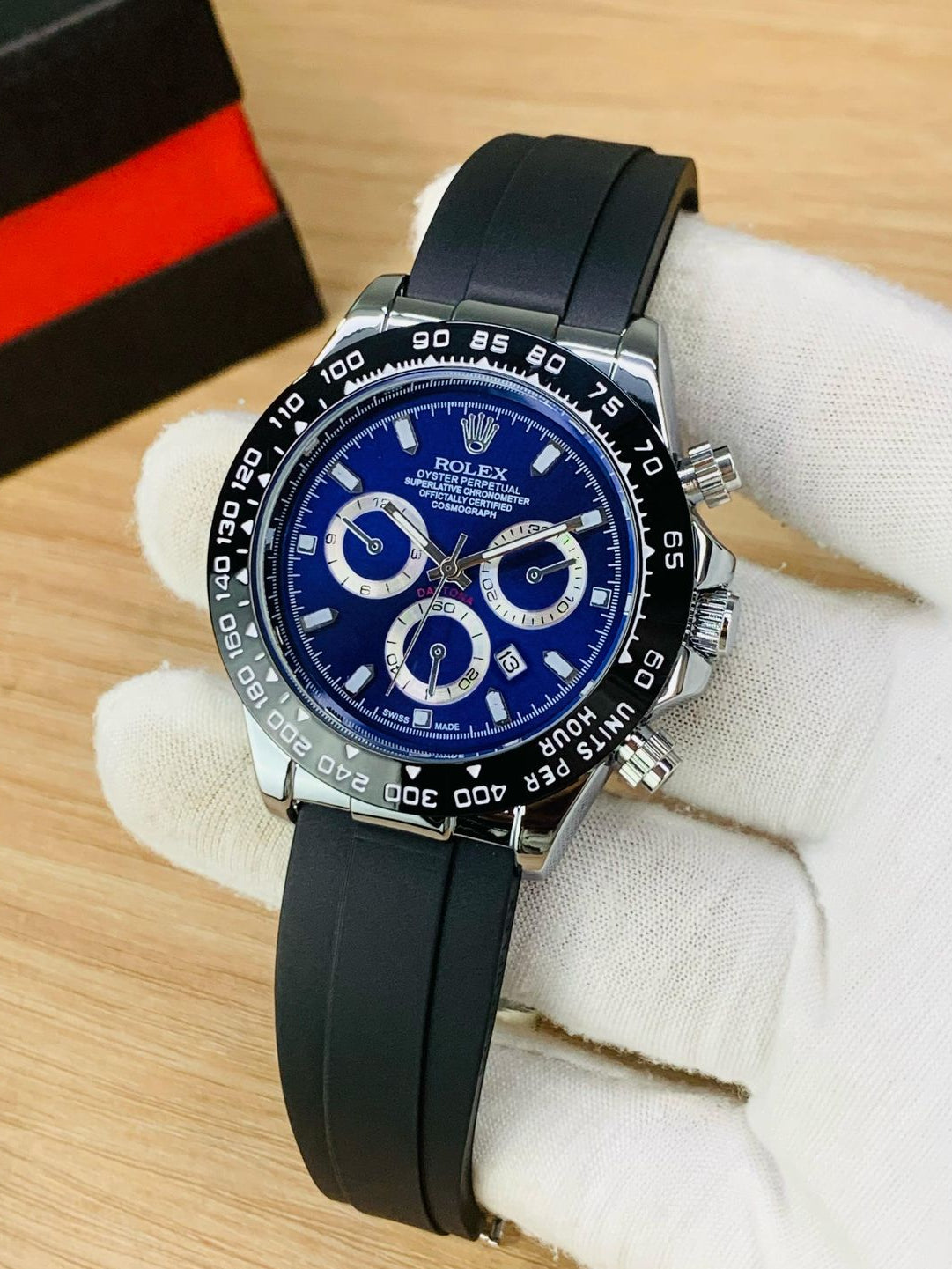 Luxury watch with blue dial and black strap on a white glove, with a blurred background.